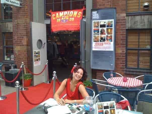 Vibrant outdoor pub event with red carpet and smiling hostess in red dress.