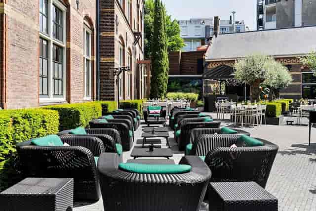Outdoor event space at The College Hotel Amsterdam with wicker seating and lush greenery.