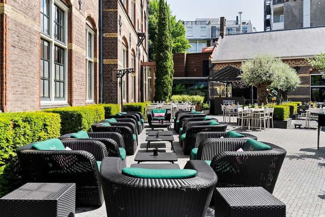 Outdoor event space at The College Hotel Amsterdam with wicker seating and lush greenery.