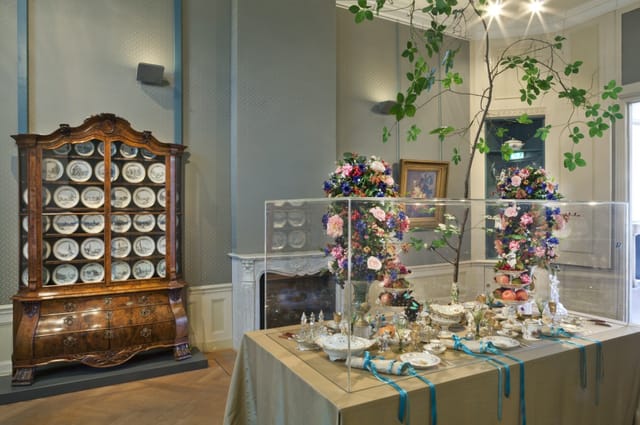 Elegant exhibition display in Cromhout House with floral arrangements and fine china.