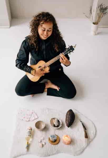 Cacao Ceremony performer with ukulele in a cozy, inviting event space.