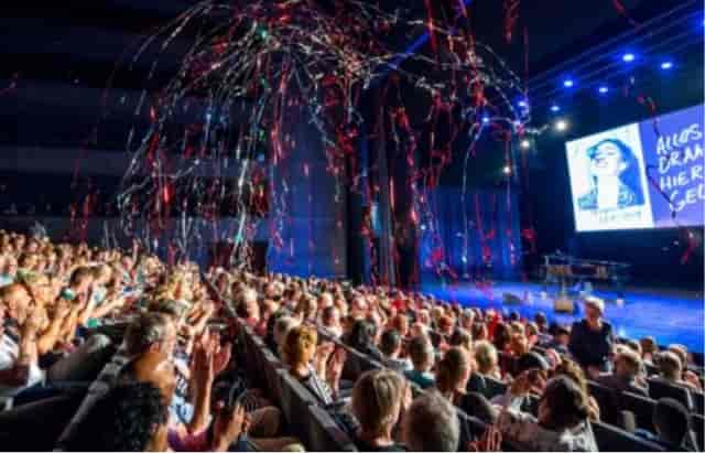 Vibrant theater event in Kunstlinie hall with enthusiastic audience and colorful streamers.