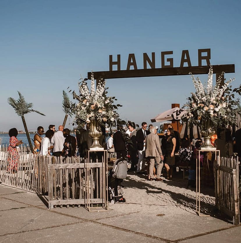 Outdoor event at HANGAR Amsterdam with floral entrance and beachside setting.