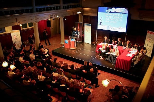 Dynamic panel discussion in Rode Hoed's Main Hall, featuring engaged audience and large screen.
