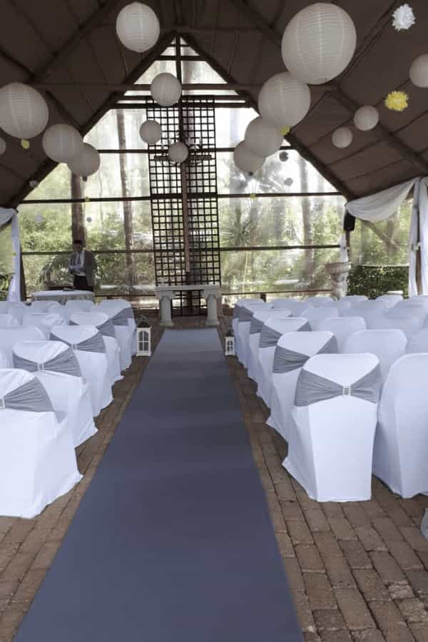 Elegant wedding venue with gray-sashed chairs and blue aisle runner in natural light.