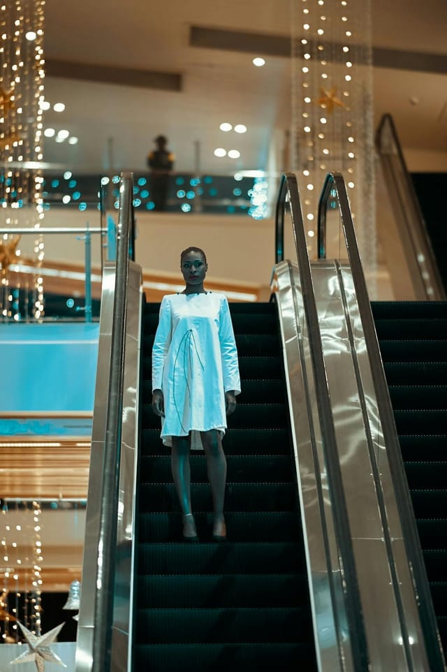 Model on escalator at Nairobi Fashion Week networking area, modern elegance, upscale event.