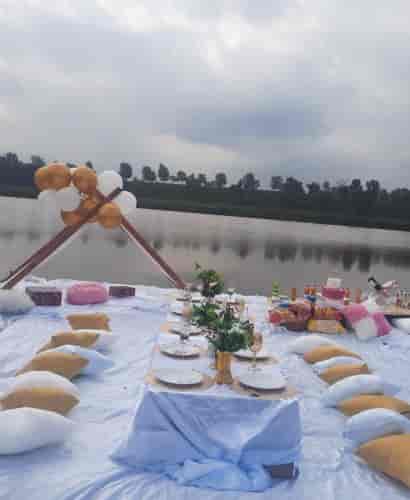 "Outdoor picnic event setup with elegant table, balloons, and serene water backdrop"