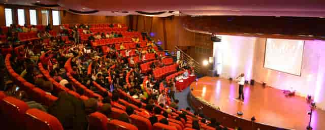 Attentive audience at a conference in tiered seating with vibrant red chairs.