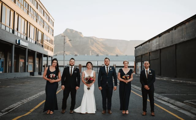 Bridal party in elegant attire at Colorbox Studios outdoor courtyard with mountain backdrop.