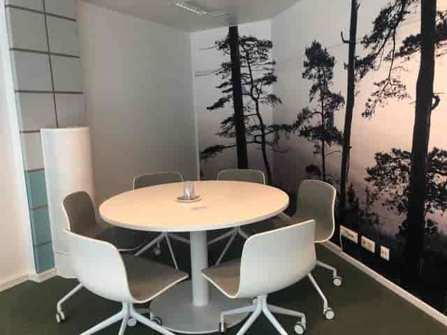 Modern meeting space with round table, ergonomic chairs, and serene tree backdrop.