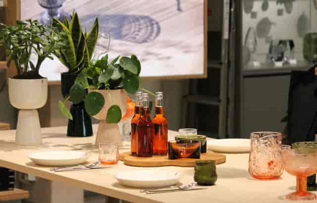 Elegant tabletop setup with greenery and beverages at Iittala Village outlet mall event.