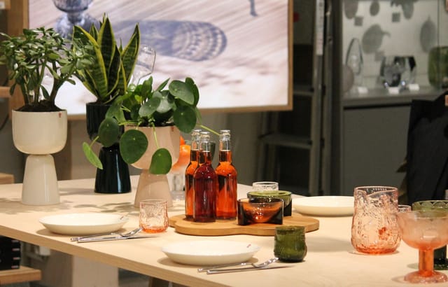 Elegant tabletop setup with greenery and beverages at Iittala Village outlet mall event.