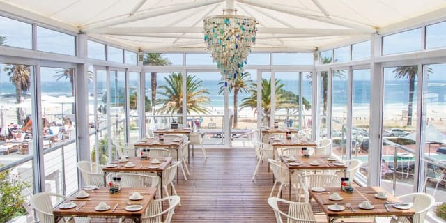 Bright beachside venue at The Bay Hotel, featuring elegant dining tables and ocean views.