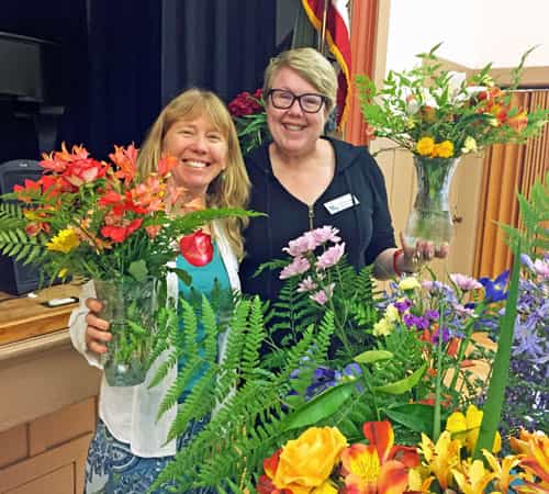 Smiling women with floral arrangements at Redwood City Woman's Club event.