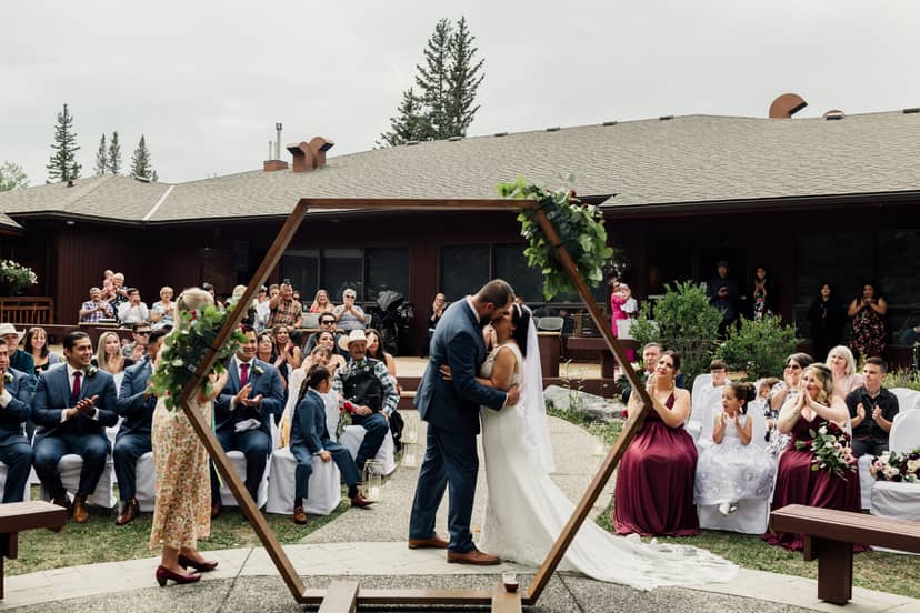 Couple kissing under hexagonal arch at a beautiful outdoor wedding in Wolf Willow Room.