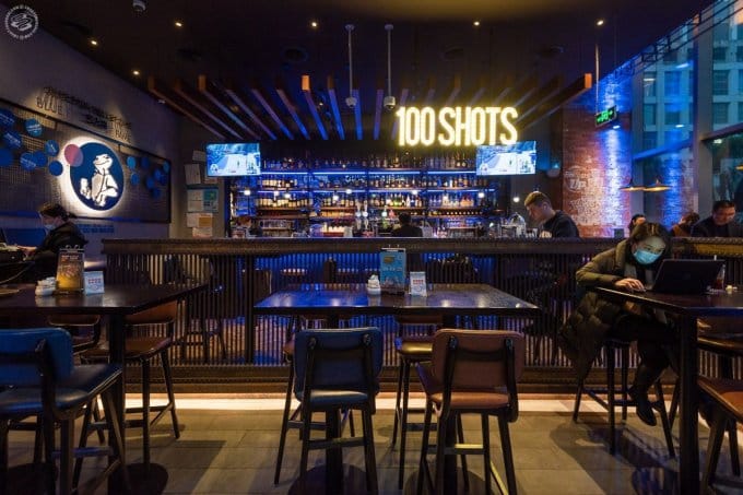 Vibrant bar in Blue Frog with "100 SHOTS" sign for casual gatherings and networking.