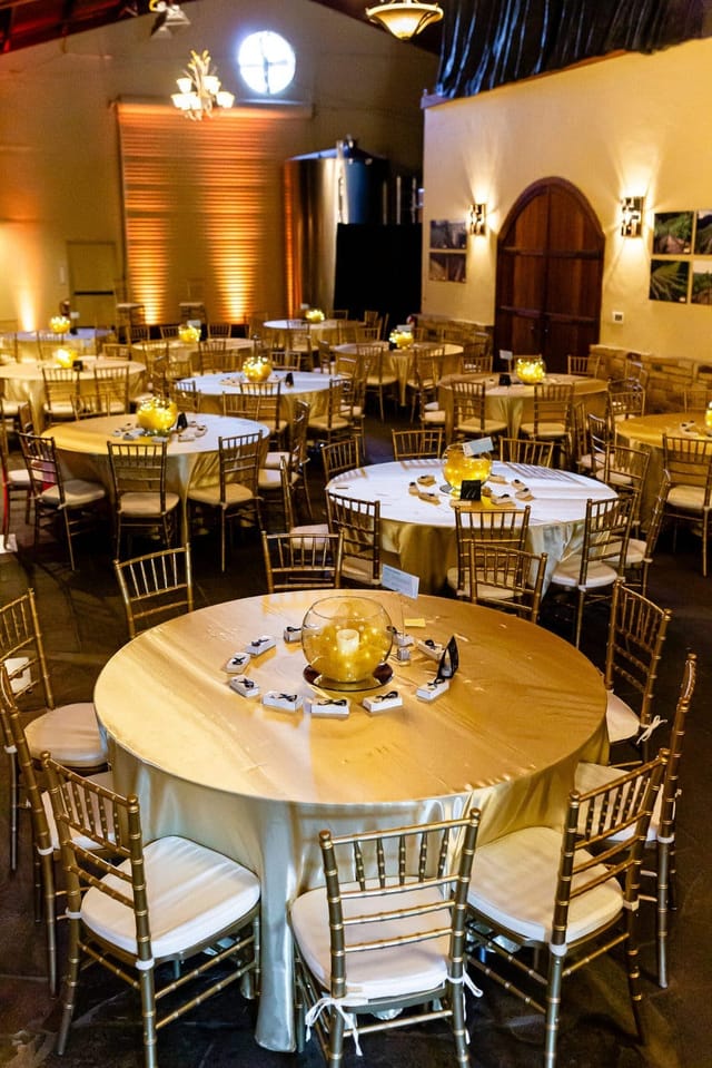 Elegant winery event space with round tables, cream linens, and gold accents. Perfect for gatherings.
