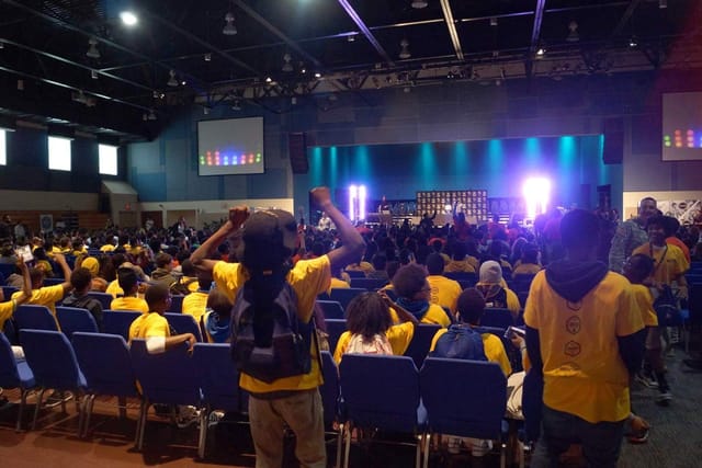 Vibrant banquet hall at KBC Houston, packed audience in yellow shirts for a conference.