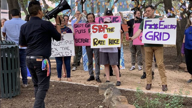 Outdoor Sierra Club meeting advocating against energy rate hike with banners and megaphones.