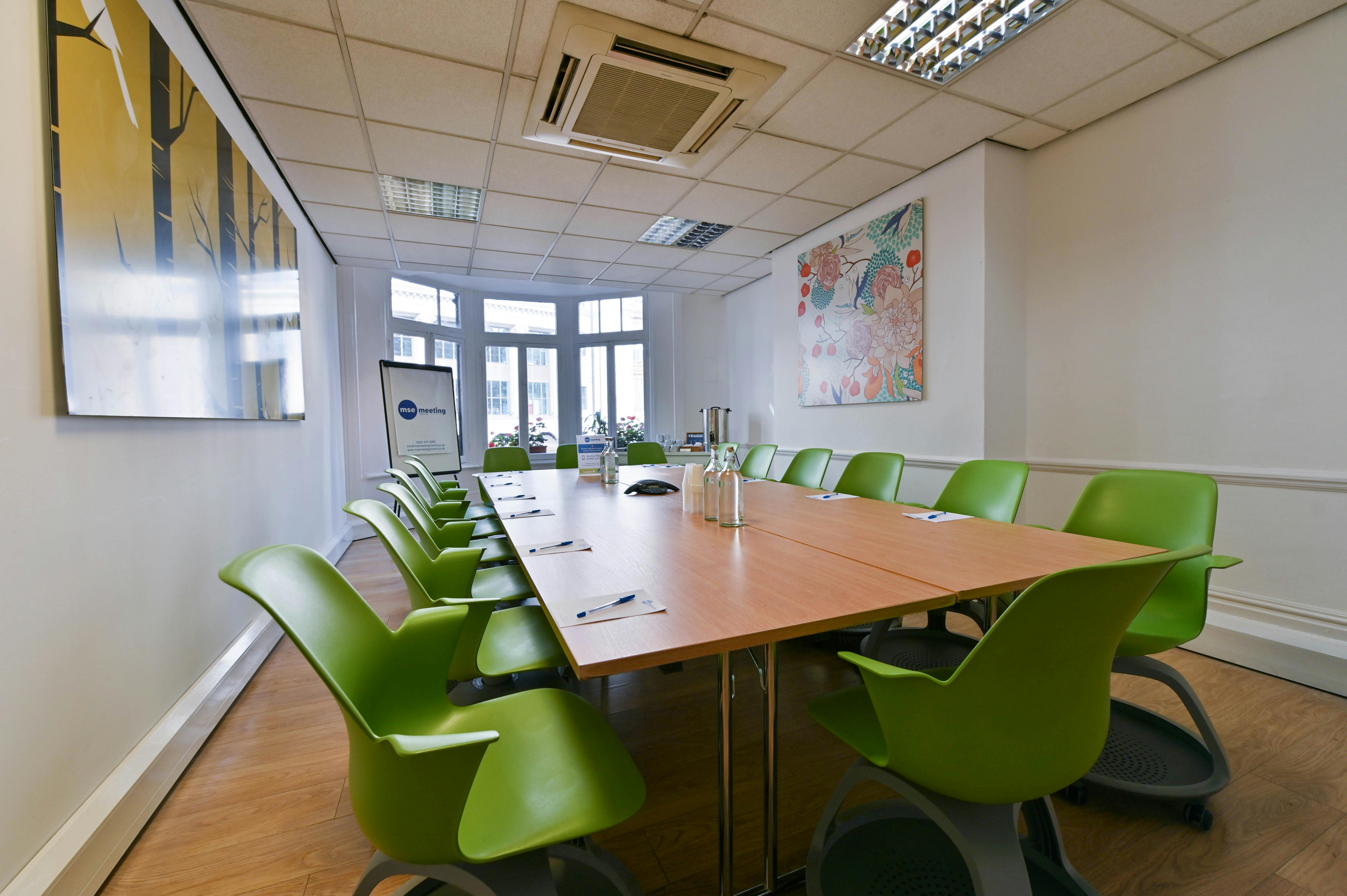 Modern meeting room with wooden table and green chairs, ideal for collaboration events.