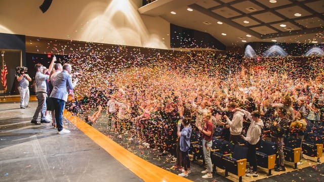 Confetti-filled audience at Flower Mound High School Theatre during vibrant event celebration