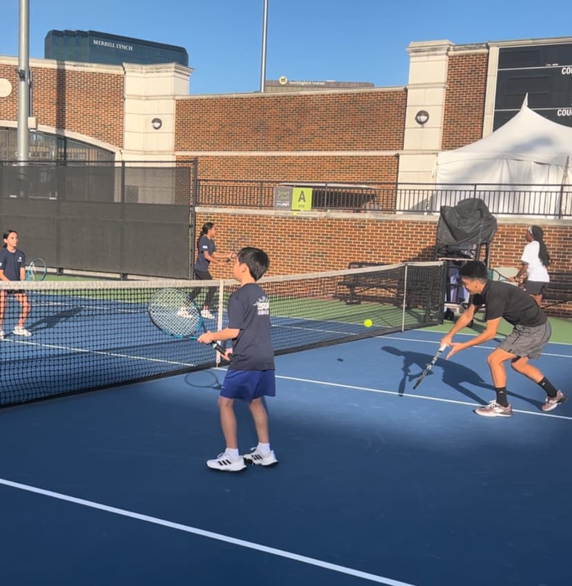 Outdoor tennis match at Dallas Athletic Club showcasing youth players and teamwork.