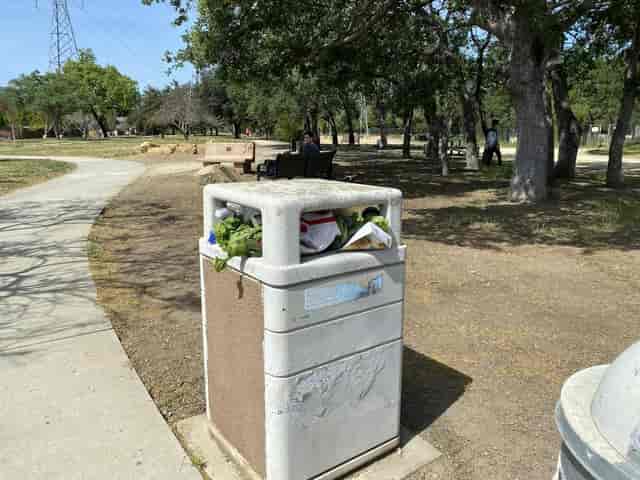 Overflowing waste bin in San José park emphasizes proper waste management during events.