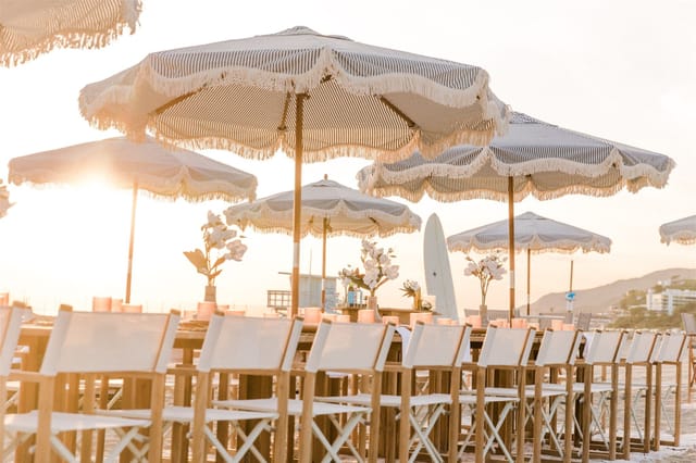 Grazing table with floral décor under umbrellas at Bliss Beach for upscale events.