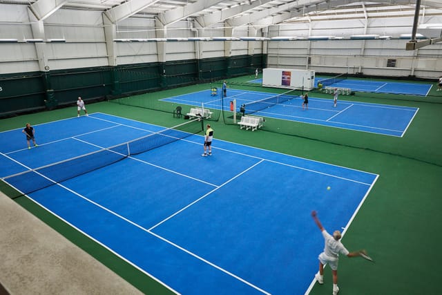 Indoor tennis facility with blue courts at Houston Racquet Club for sports events and tournaments.