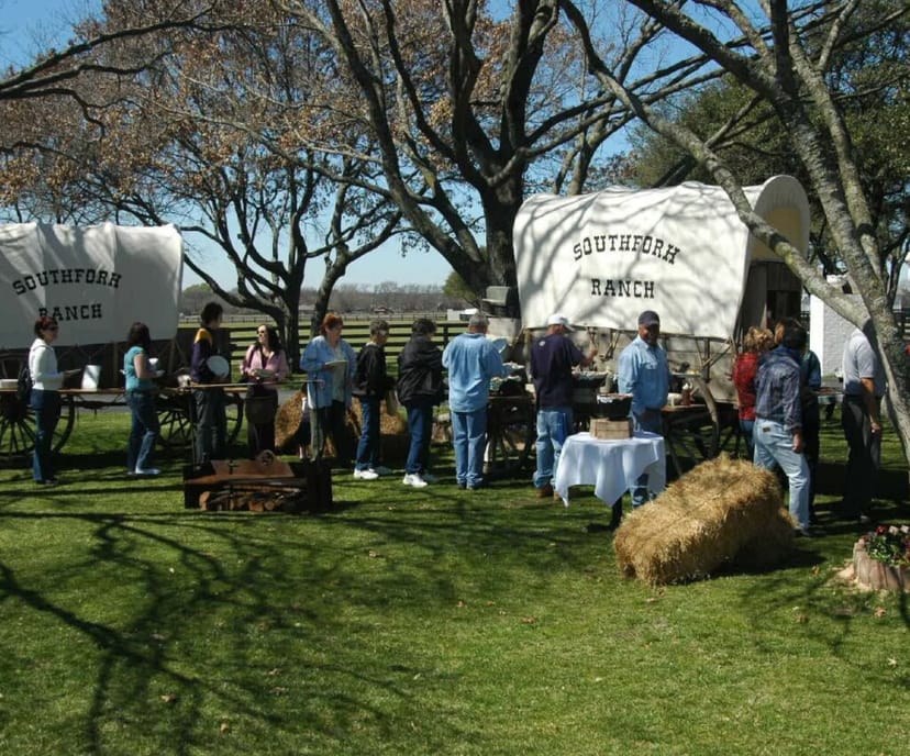 Lively outdoor networking event at Southfork Ranch with vintage wagons and trees.