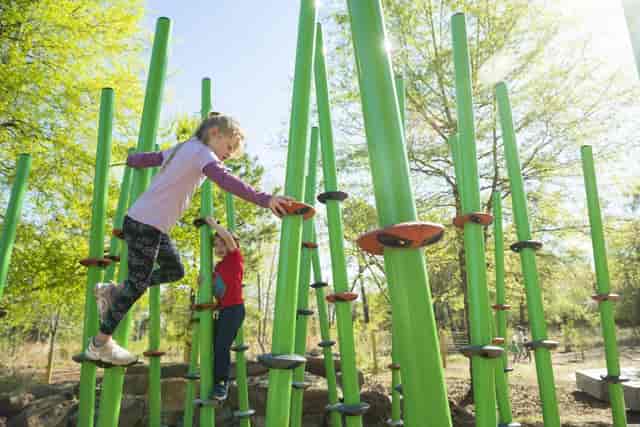 Children climbing colorful structures at Houston Arboretum for team-building activities.
