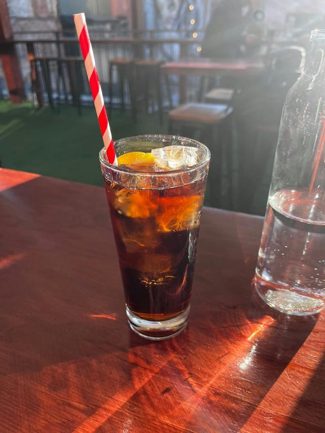 Refreshing iced drink with orange garnish at The Emerald Peacock indoor bar.