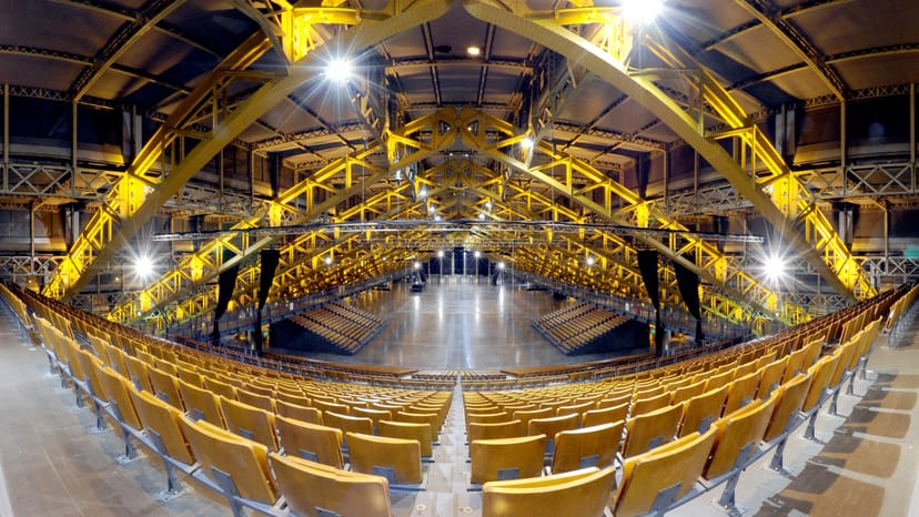 Industrial event space with tiered seating and yellow beams, ideal for conferences and concerts.