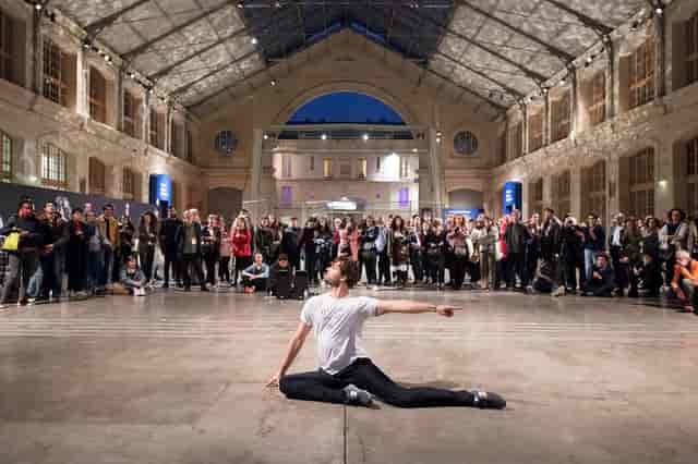 "Perfomer captivating audience in vibrant CENTQUATRE-PARIS theater event atmosphere."