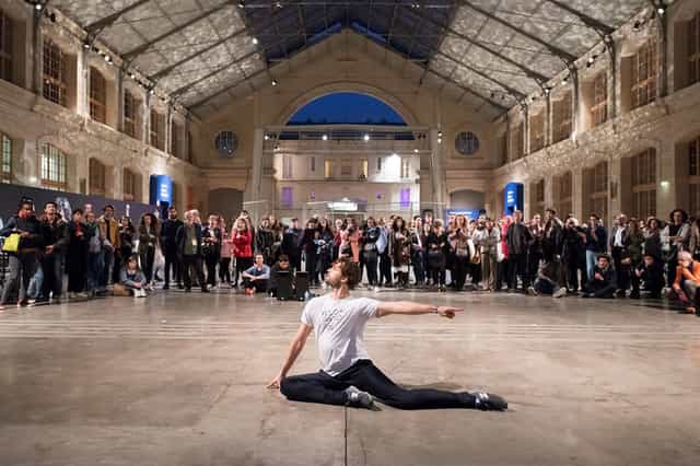"Perfomer captivating audience in vibrant CENTQUATRE-PARIS theater event atmosphere."