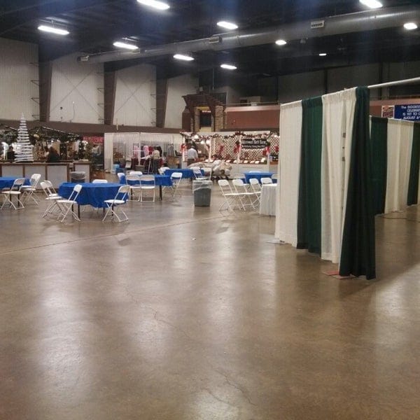 Spacious event center at The Fairgrounds, set for trade show with blue tables and chairs.
