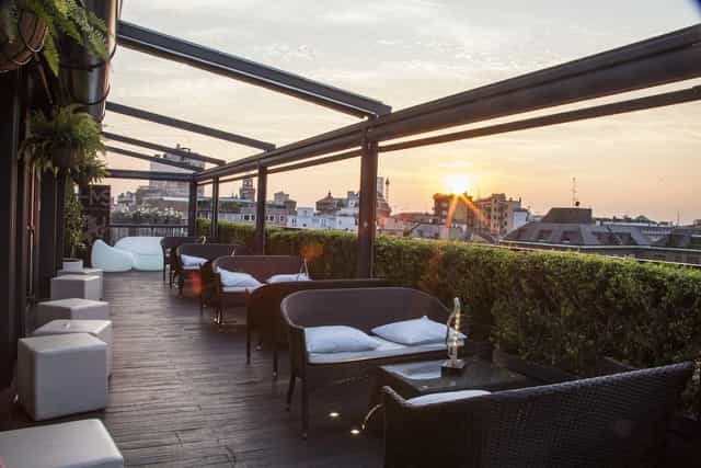Milan rooftop lounge, cocktail reception, sunset skyline.
