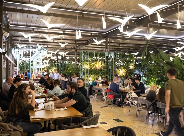 Biophilic restaurant terrace with avian lighting for group dining and corporate mixers.
