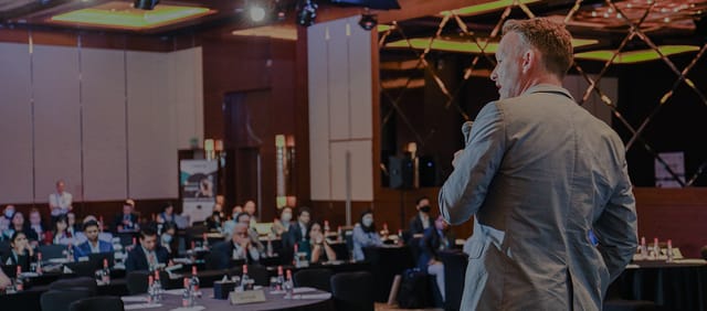 Speaker at MoRE 2.0 Conference in a boardroom-style hotel ballroom event.