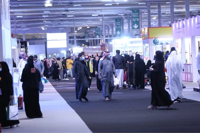 Bustling trade show exhibition hall at Riyadh Front, featuring professional wayfinding signage.