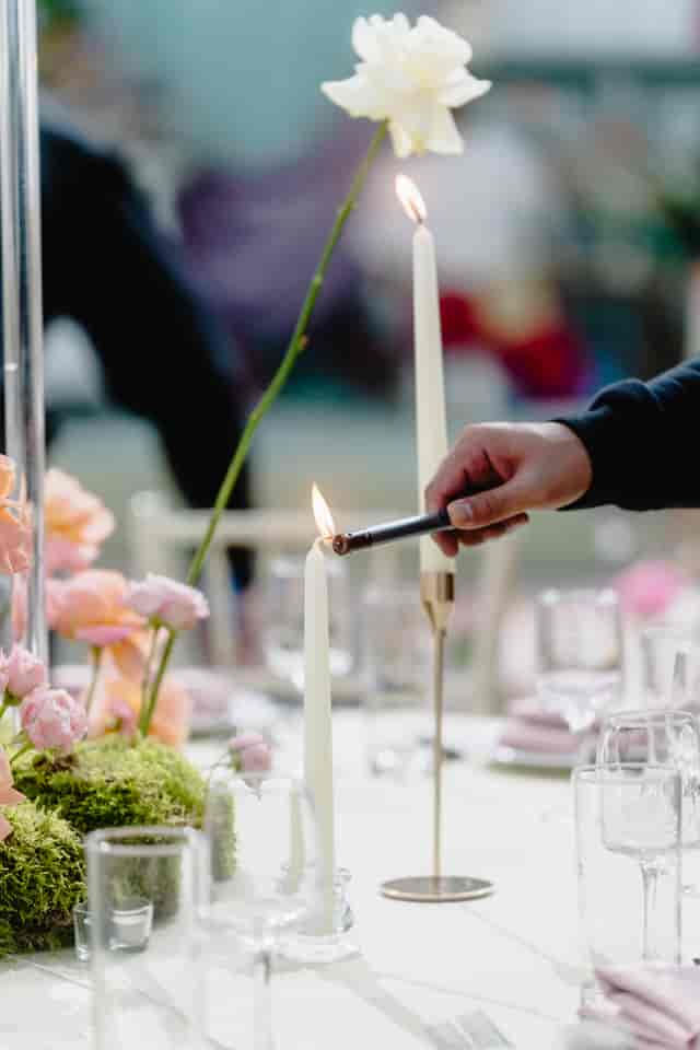 Hand lighting taper candle at elegant table with pink flowers for sophisticated event ambiance.
