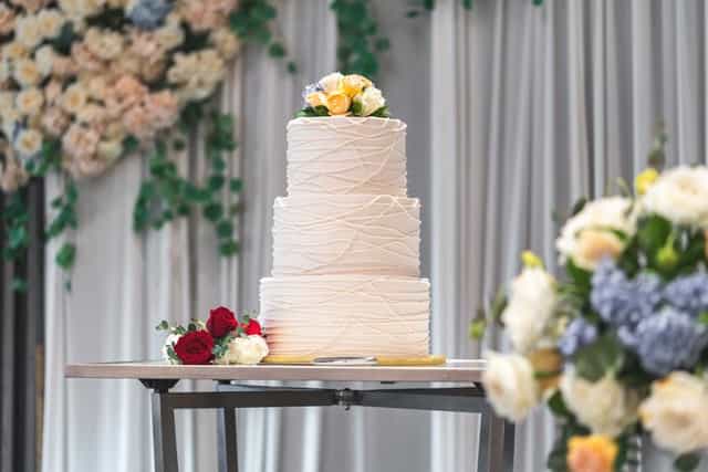 Elegant wedding cake display with floral arrangements at Village Square event center.