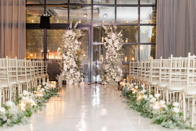Grand Estate Ballroom wedding ceremony with floral pillars and white Chiavari chairs.