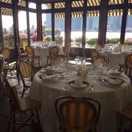 Sun-drenched River Cafe banquet hall with round tables for elegant waterfront corporate events.