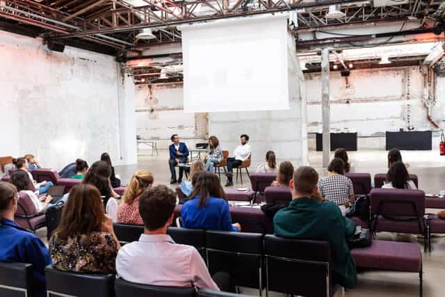 Industrial chic panel discussion venue in Tokyo with modular seating and projection screen.