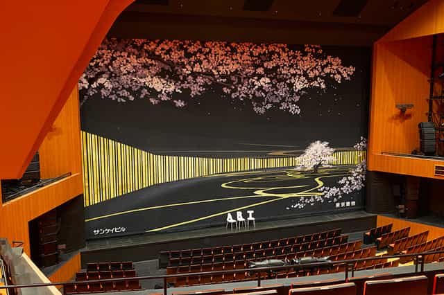 Brillia Hall proscenium stage with scenic backdrop for keynote and panel discussion events.