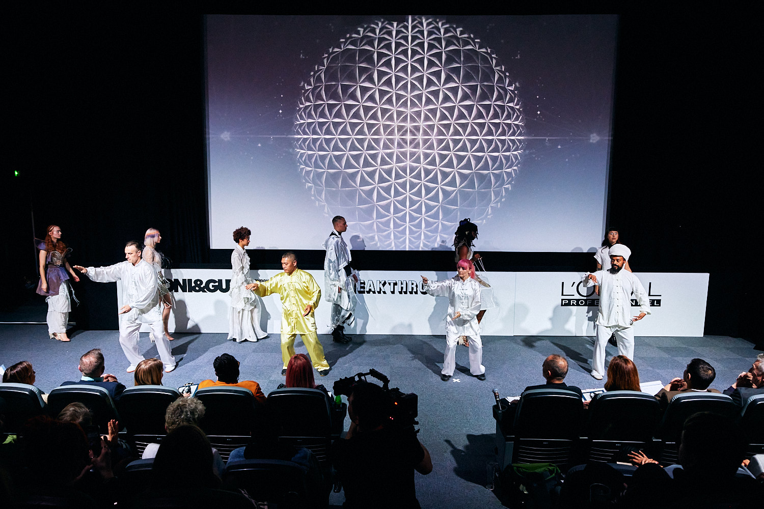 Dynamic stage performance at Riverside Studios with vibrant costumes and geometric backdrop. - Banner