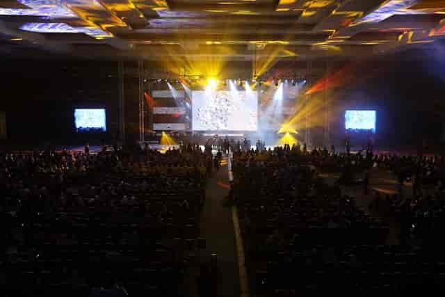 Theater-style general session in convention center with massive LED screen and truss lighting.