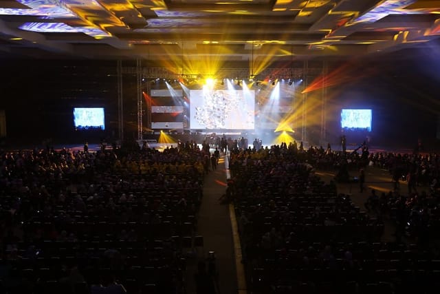 Theater-style general session in convention center with massive LED screen and truss lighting.