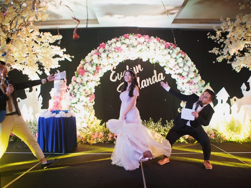 Emcee duo at Holiday Inn Jakarta Gajah Mada event with floral stage backdrop for business meetings.